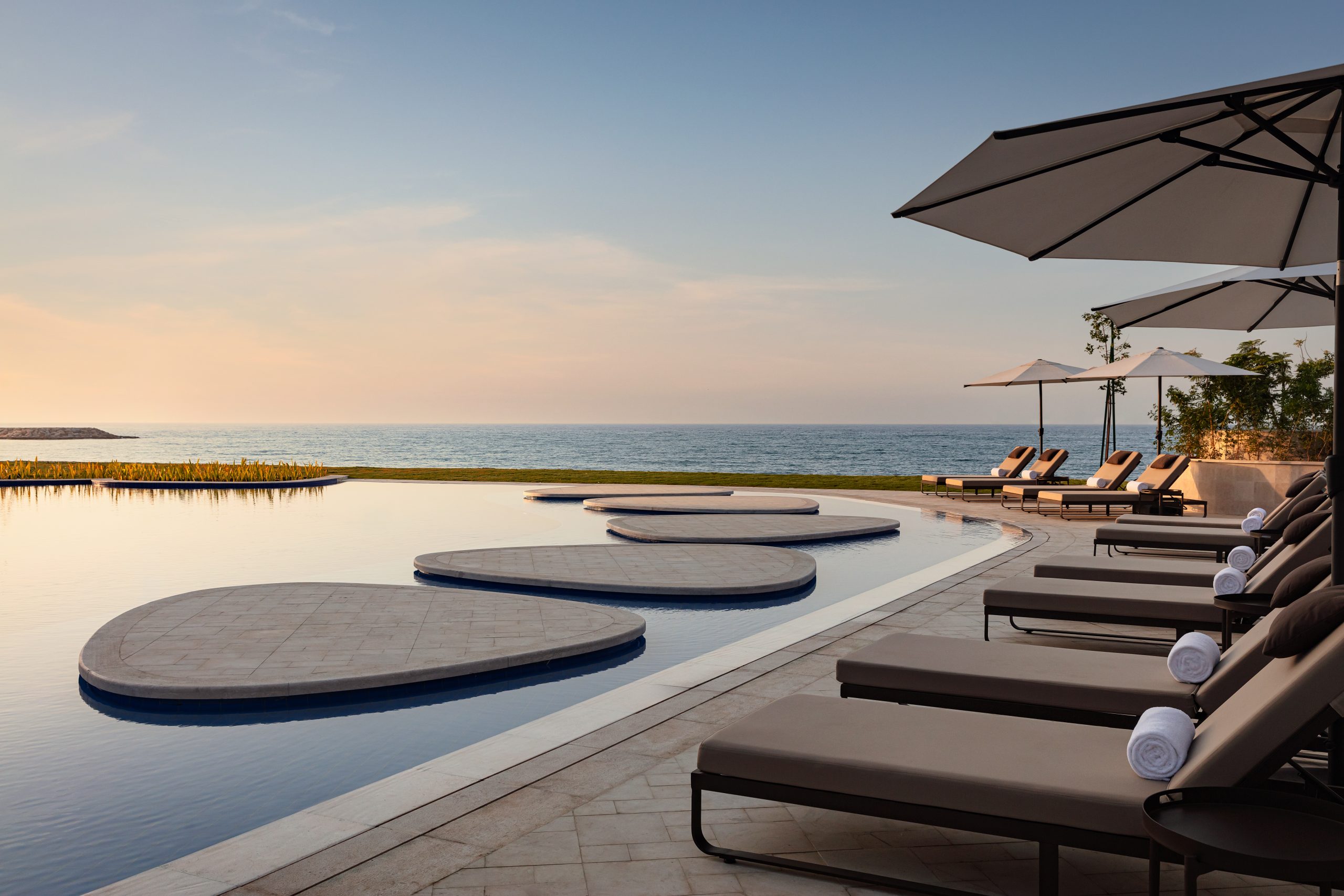 Sunset pool with loungers and umbrellas by the sea.