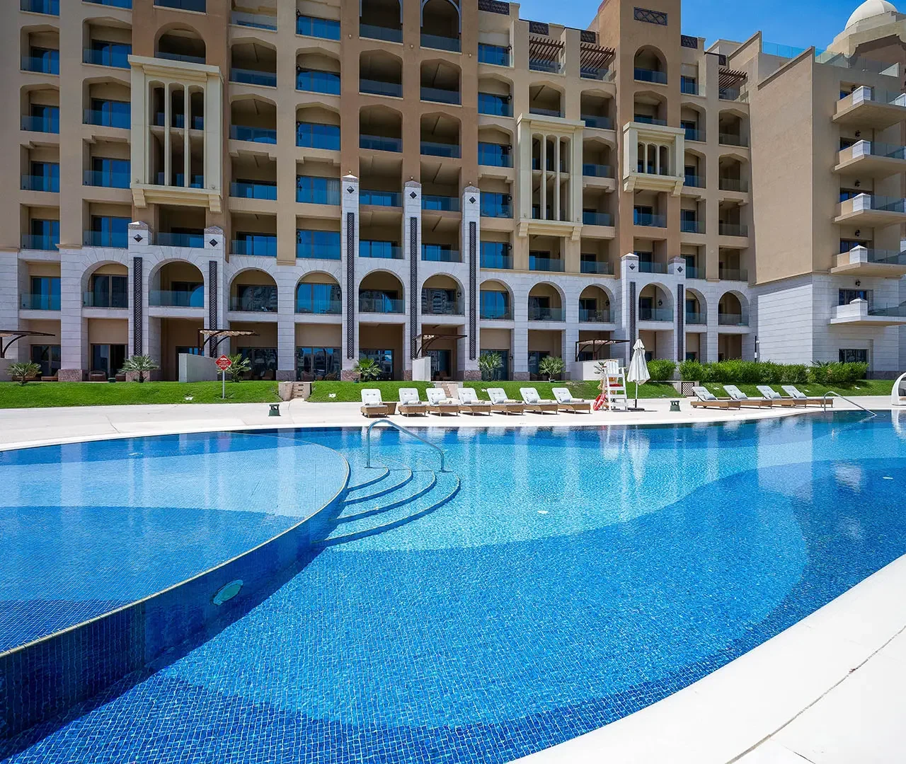 Large curved pool by luxury apartment building.